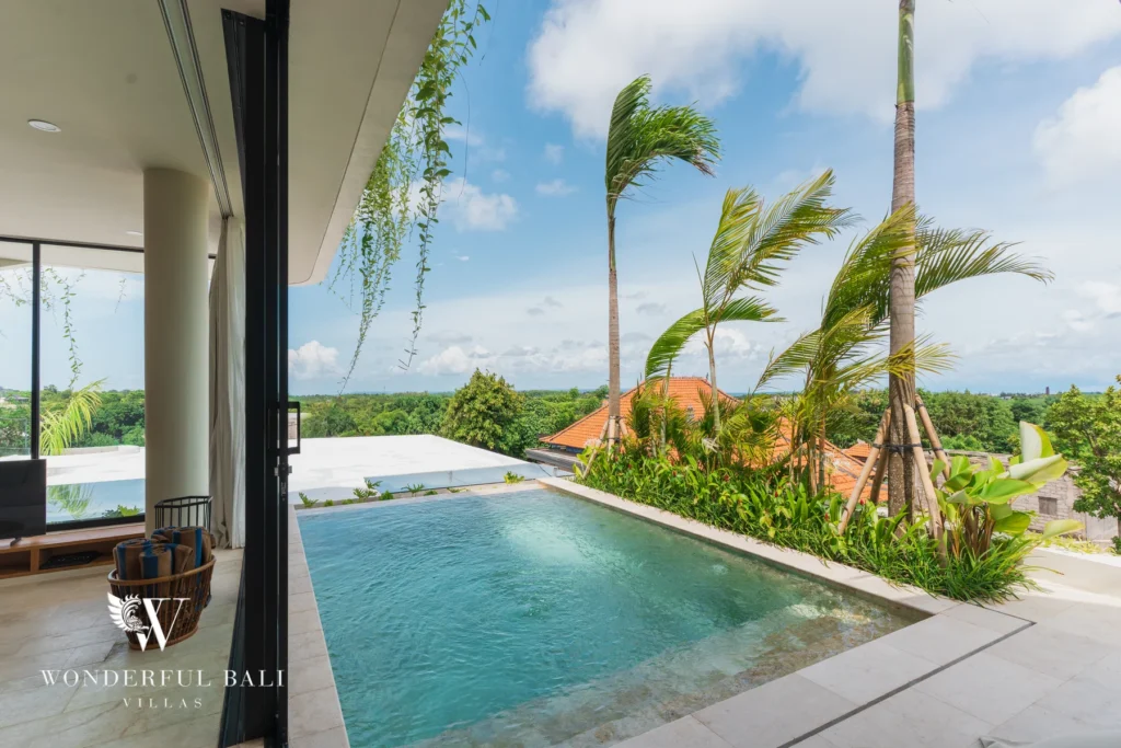 A private pool bordered by swaying palm trees and tropical planting with sliding glass doors and open views to the horizon at a 3-bedroom villa in Bingin, Uluwatu, Bali