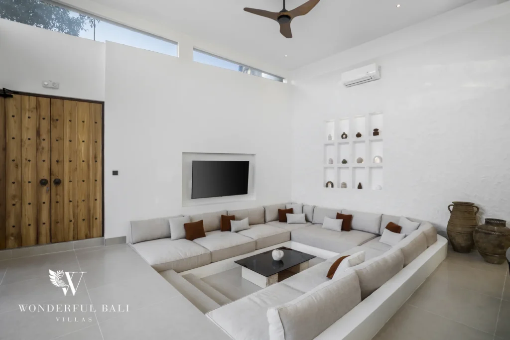 A living room with a trendy sunken sofa, wall-mounted TV and carved wooden doors under high ceilings at a 3-bedroom villa in Bingin, Uluwatu, Bali