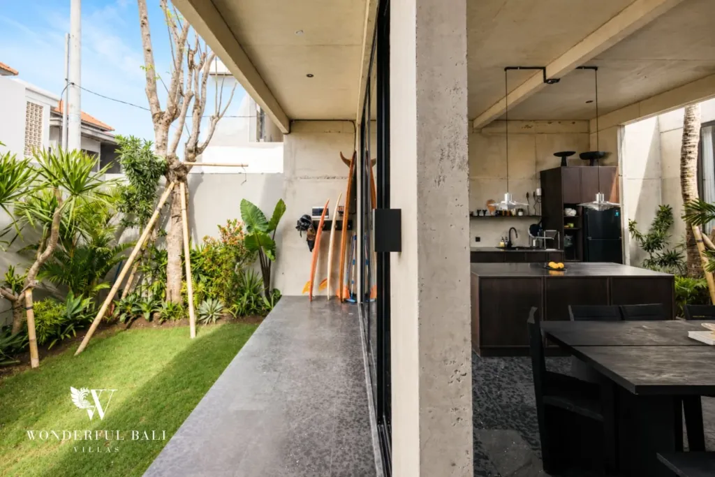 Polished concrete side deck with surfboards lined against the wall and sliding glass doors opening onto the kitchen and dining area at a 2-bedroom villa in Seseh, Bali