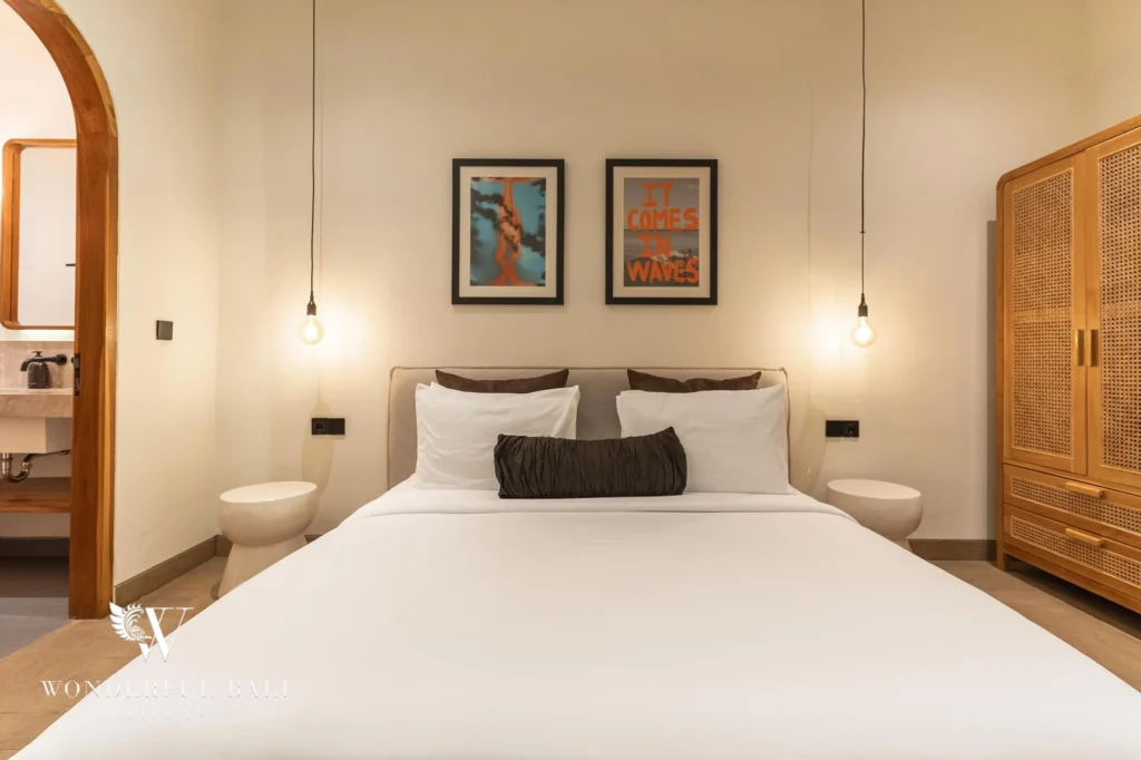 A bedroom at night with pendant bulbs, framed surf posters and an en-suite bathroom through an arched doorway at a 2-bedroom villa in Canggu, Bali