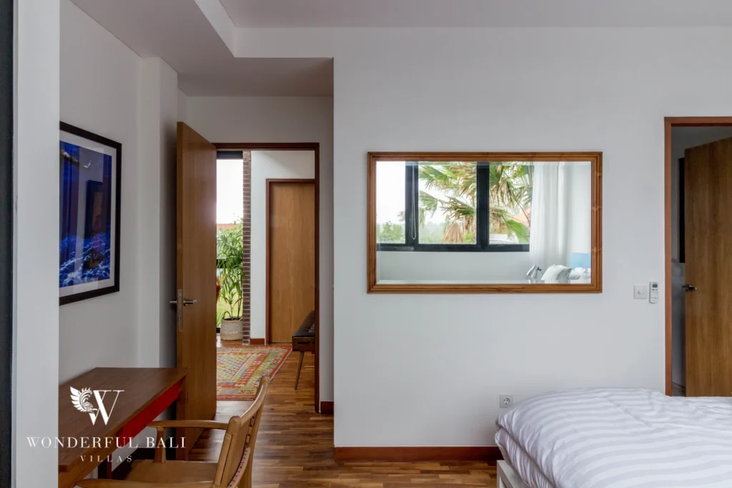 A bedroom with a timber desk, wall mirror and an open doorway leading to a planted terrace over timber floors at a 4-bedroom villa in Batu Bolong, Canggu, Bali