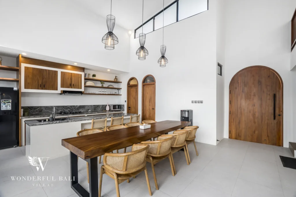 Timber dining table and open kitchen with arched doors at a 3-bedroom villa in Pererenan, Bali