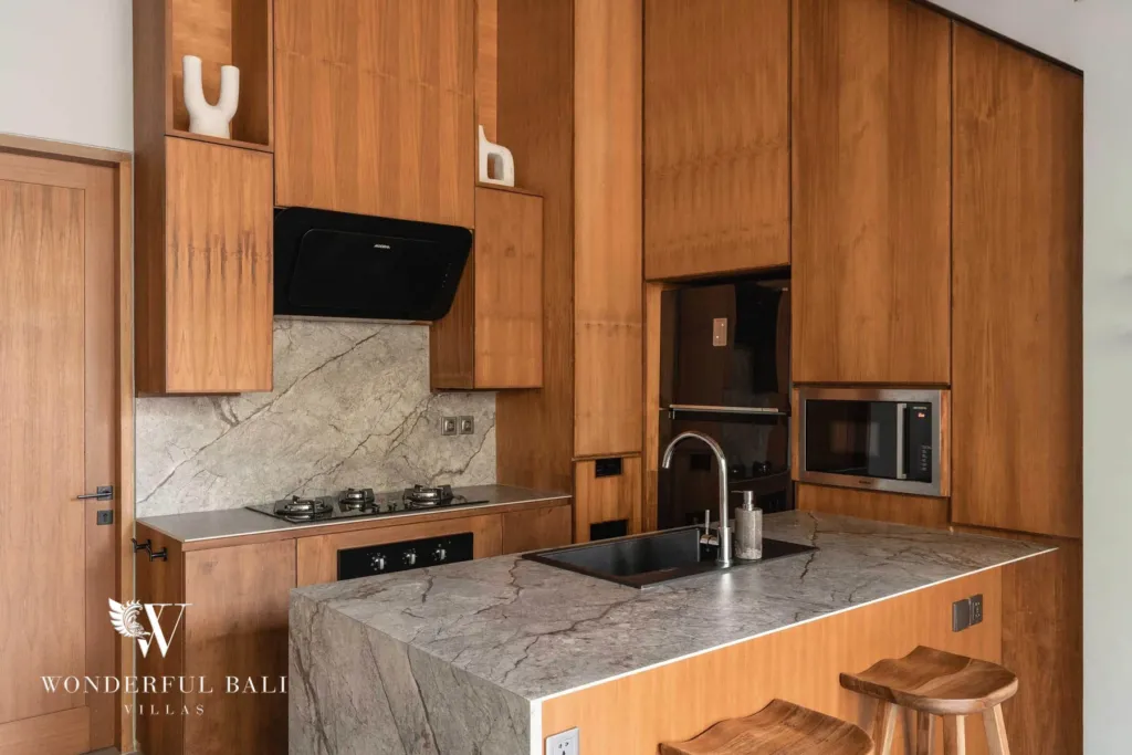 2BR villa for rent in Pererenan — kitchen, a close view of the kitchen's marbled stone island with a black sink, gas hob, built-in microwave and timber bar stools at a 2-bedroom villa