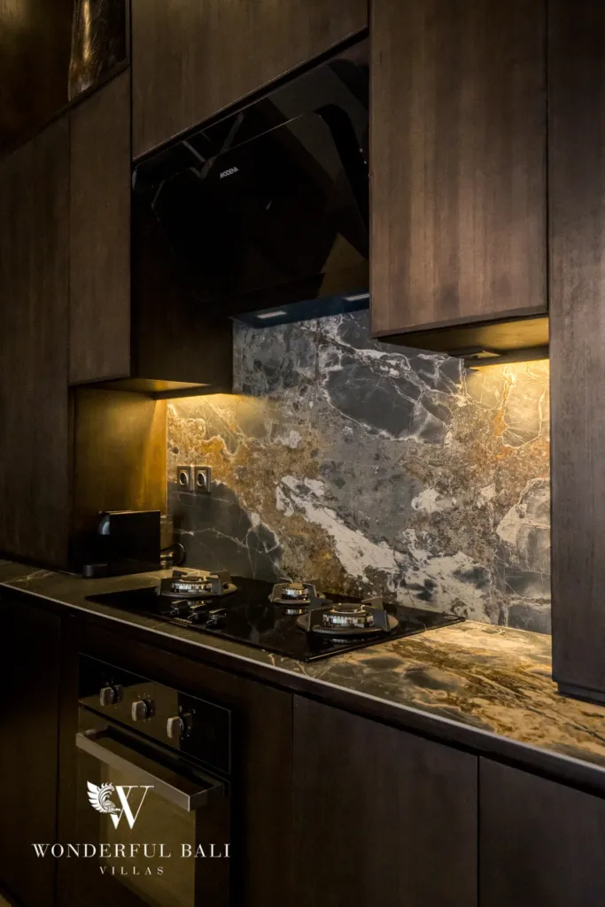 2BR villa for rent in Pererenan — kitchen, a close-up of the kitchen gas cooktop, oven and dramatic veined marble backsplash in dark wood cabinetry at a 2-bedroom villa