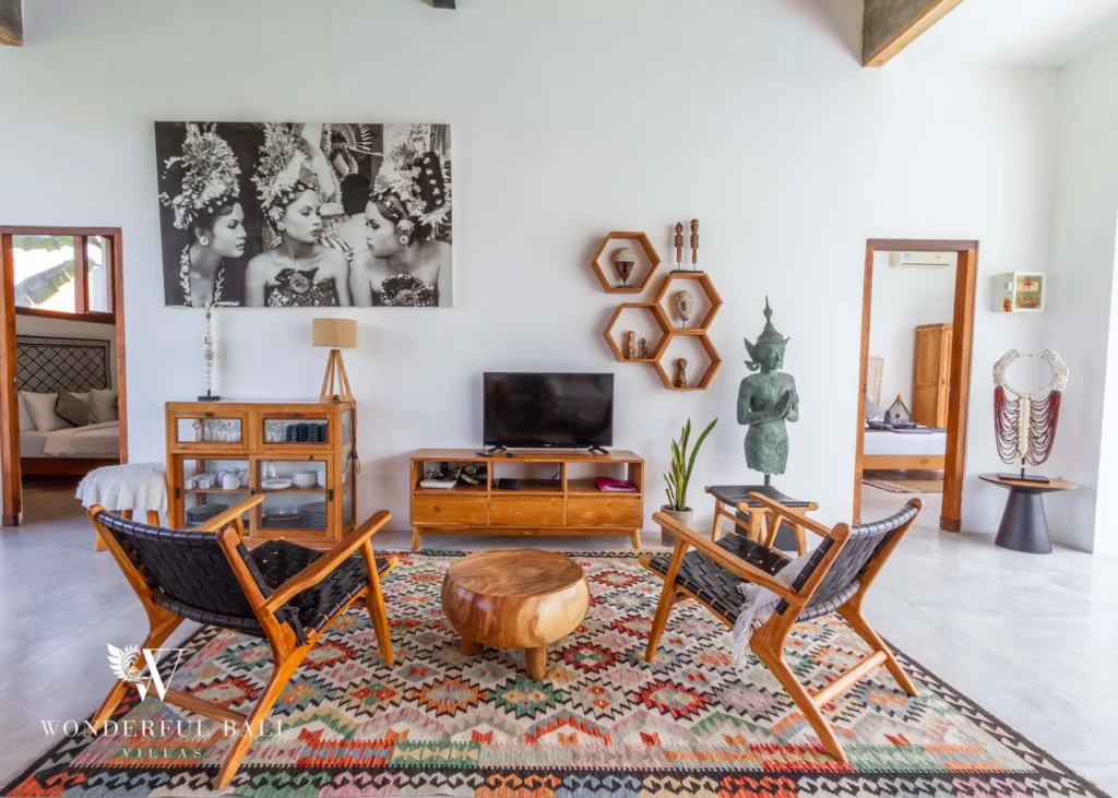 A bright sitting area with timber chairs, a smart TV on a wooden console and a large photographic artwork between two bedroom doorways at a 3-bedroom villa in Seminyak, Bali