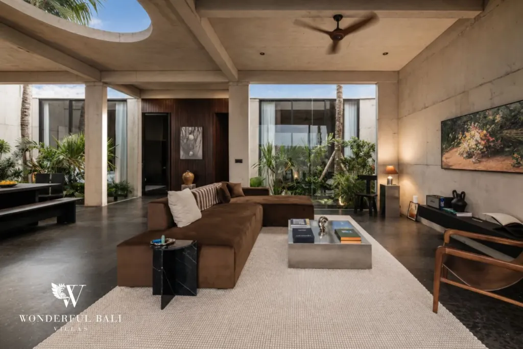 Spacious living lounge with a large brown sectional sofa, concrete coffee table and floor-to-ceiling glazing onto a planted courtyard at a 2-bedroom villa in Seseh, Bali