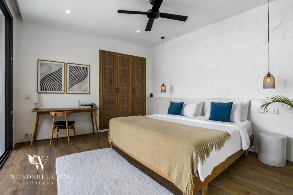 Boho bedroom with a wooden bed, rattan wardrobe, a desk with framed art and a black ceiling fan at a 3-bedroom villa in Bingin, Uluwatu, Bali