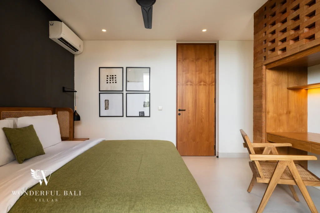 A bedroom with a cane headboard, olive-green bedspread, framed prints, a timber desk and chair and a latticed wood shelving unit at a 5-bedroom villa in Batu Bolong, Canggu, Bali