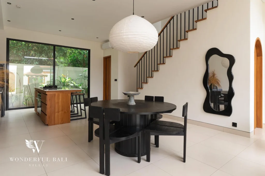 An indoor dining area with a round black table and chairs beside the staircase and open kitchen at a 2-bedroom villa in Canggu, Bali