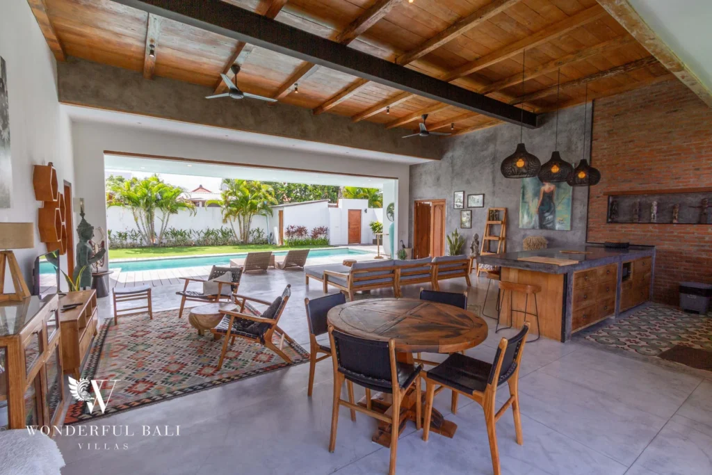 A covered dining and lounge terrace with a round timber table, leather chairs and a bar counter overlooking the pool at a 3-bedroom villa in Seminyak, Bali