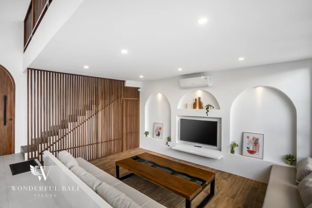 Family lounge with arched wall niches and timber-slat staircase at a 3-bedroom villa in Pererenan, Bali