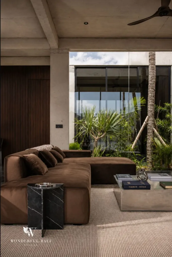 Close view of the brown suede sectional sofa, black marble side table and concrete coffee table beside a palm-filled courtyard at a 2-bedroom villa in Seseh, Bali