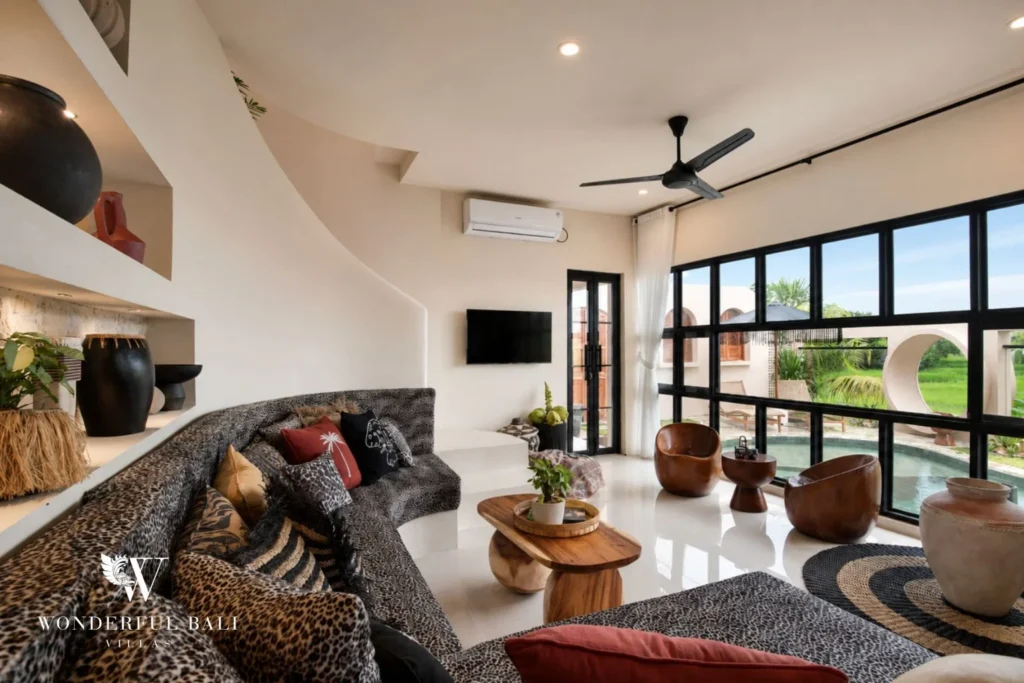A cozy living lounge with patterned sofas and wooden chairs facing the rice-field windows at a 3-bedroom villa in Pererenan, Bali