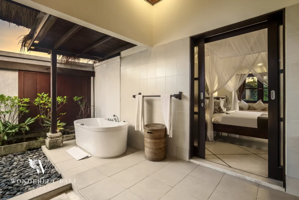 A freestanding outdoor bathtub beside a garden opening to a canopy bedroom at sunset at a 4-bedroom villa in Seminyak, Bali