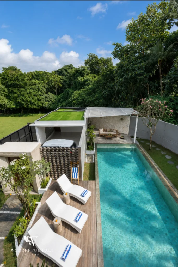 An elevated view over the pool, sun loungers and rooftop lawn surrounded by dense green trees at a 4-bedroom villa in Pererenan, Bali