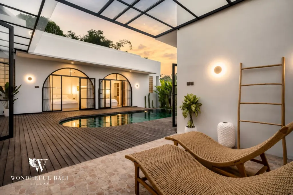 Rattan loungers on a stone terrace overlook the pool and twin arched bedroom doors at golden hour at a 3-bedroom villa in Pererenan, Bali