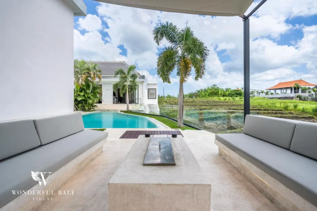 Covered outdoor terrace with cushioned bench seating and a low table facing the pool and rice fields at a 5-bedroom villa in Pererenan, Bali