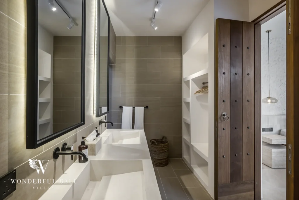 A bathroom with a double stone vanity, framed mirrors, open shelving and a carved wooden door at a 3-bedroom villa in Bingin, Uluwatu, Bali