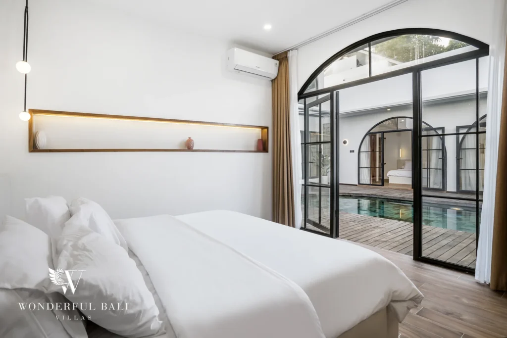 Bedroom with arched glass doors and pool view at a 3-bedroom villa in Pererenan, Bali