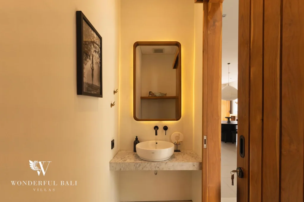 A guest powder room with a round vessel sink, backlit mirror and warm lighting at a 2-bedroom villa in Canggu, Bali