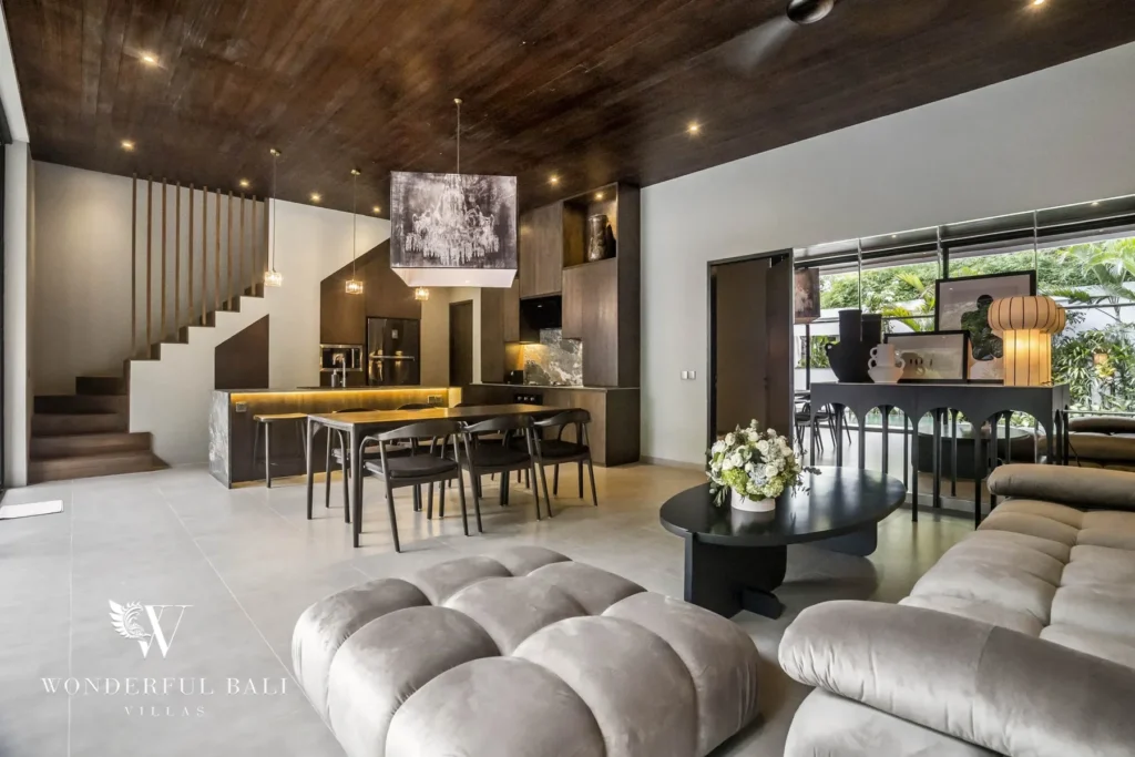 An open living area with plush velvet sofas, a staircase, dining table and kitchen bar beneath a dark wood ceiling at a 3-bedroom villa in Pererenan, Bali
