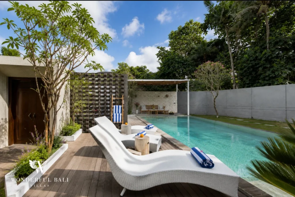 Twin white loungers on the timber pool deck with striped towels beside the turquoise pool and garden at a 4-bedroom villa in Pererenan, Bali