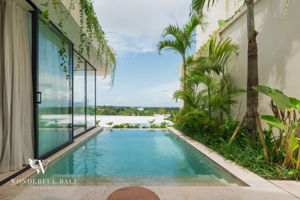 A slim private pool running between the villa wall and a planted border of palms with open views beyond at a 3-bedroom villa in Bingin, Uluwatu, Bali