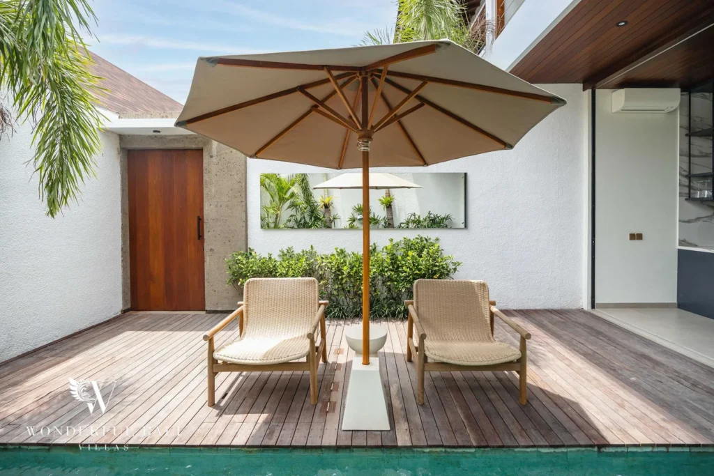 Two rattan sun loungers under a canvas umbrella on a wooden deck beside the pool at a 2-bedroom villa in Canggu, Bali