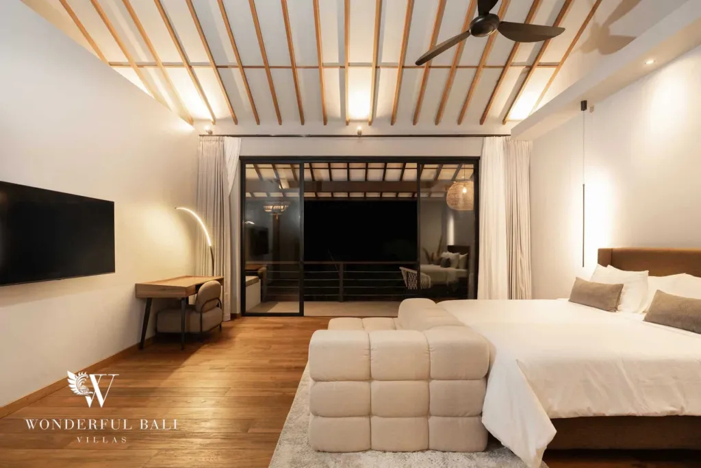 2BR villa for rent in Pererenan — bedroom, a bedroom lit at night with a warm glow, TV, writing desk and cream daybed opening through glass doors to a dark balcony at a 2-bedroom villa