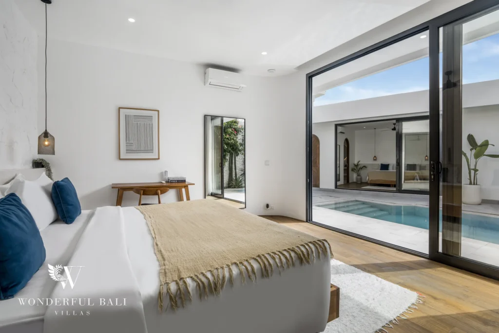 Bedroom with a textured white headboard wall, wooden bed, standing mirror and a desk on timber flooring at a 3-bedroom villa in Bingin, Uluwatu, Bali