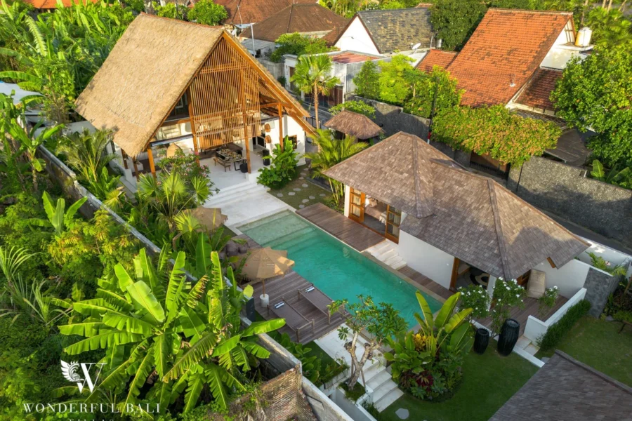 An aerial view shows the thatched pavilion, shingle-roofed bungalows and a private pool surrounded by dense tropical greenery at a 4-bedroom villa in Canggu, Bali