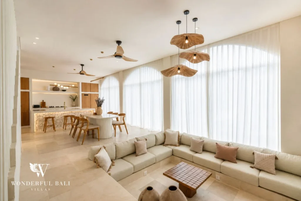 A bright open-plan living and dining space with a long sectional sofa, dining table and tall curtained windows, at a 2-bedroom villa in Bingin, Uluwatu, Bali