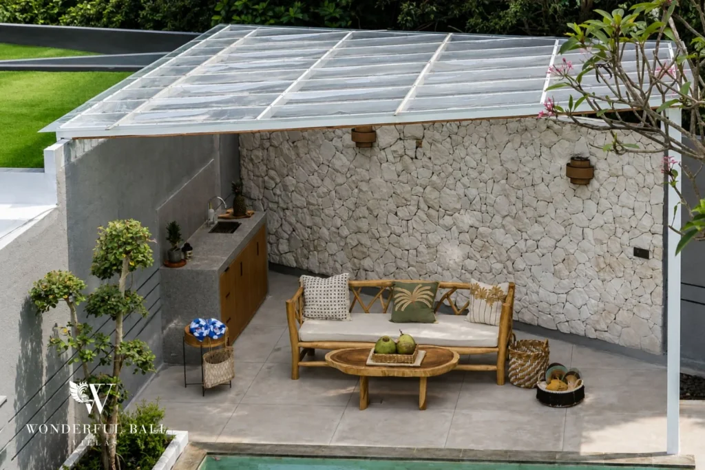A stone-walled covered outdoor lounge with a rattan sofa and round timber coffee table beside the pool at a 4-bedroom villa in Pererenan, Bali