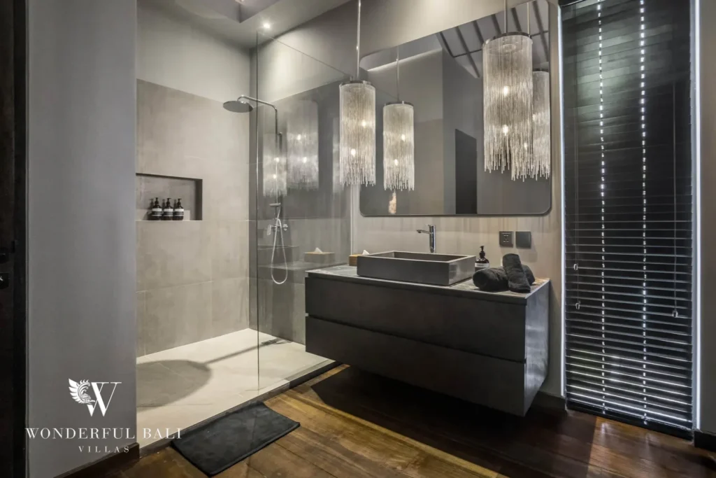 A bathroom with a glass walk-in rain shower, a stone vessel sink on a dark vanity and pendant lighting over timber floors at a 3-bedroom villa in Pererenan, Bali