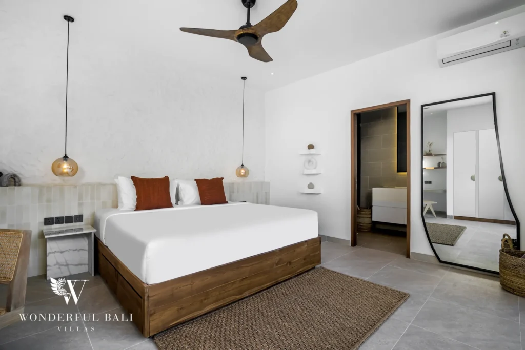A bedroom with a wooden-framed bed, globe pendant lights, a full-length mirror and an ensuite bathroom at a 3-bedroom villa in Bingin, Uluwatu, Bali