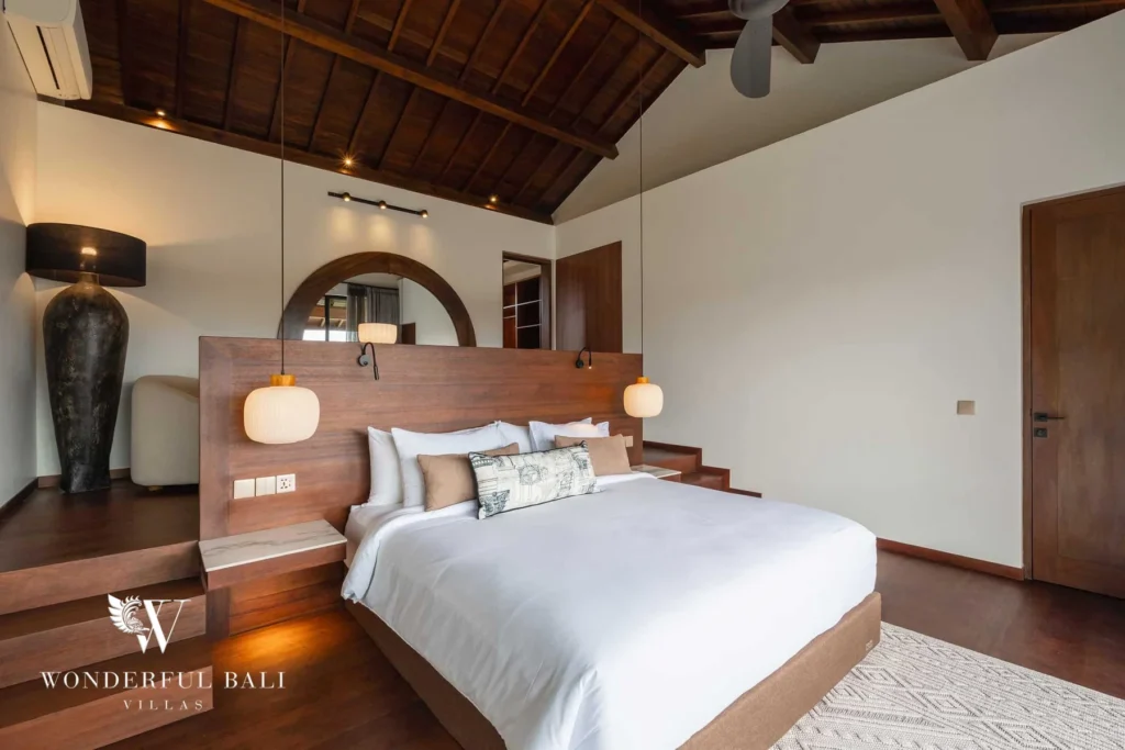 A bedroom with a king bed on a raised wooden platform, round arched mirror and vaulted timber ceiling at a 2-bedroom villa in Canggu, Bali