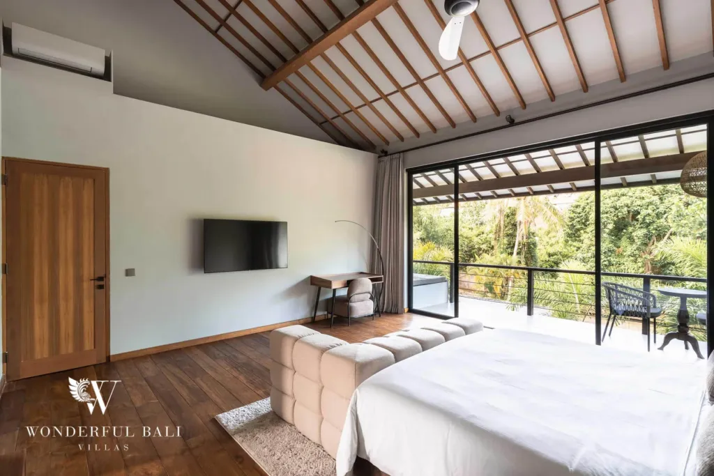 2BR villa for rent in Pererenan — bedroom, a bedroom under a vaulted timber-beam ceiling with sliding glass doors opening to a private balcony and lush garden view at a 2-bedroom villa