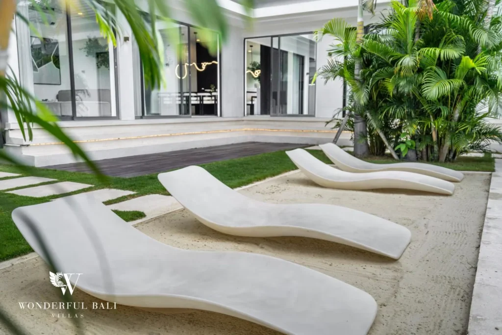 Curved white loungers arranged on the lawn and sand in the landscaped garden beside the villa at a 5-bedroom villa in Pererenan, Bali