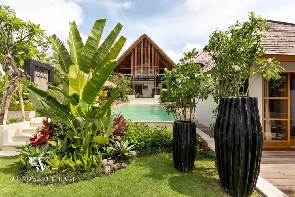 A landscaped garden with banana plants and tall black planters leads past the pool toward the timber pavilion at a 4-bedroom villa in Canggu, Bali