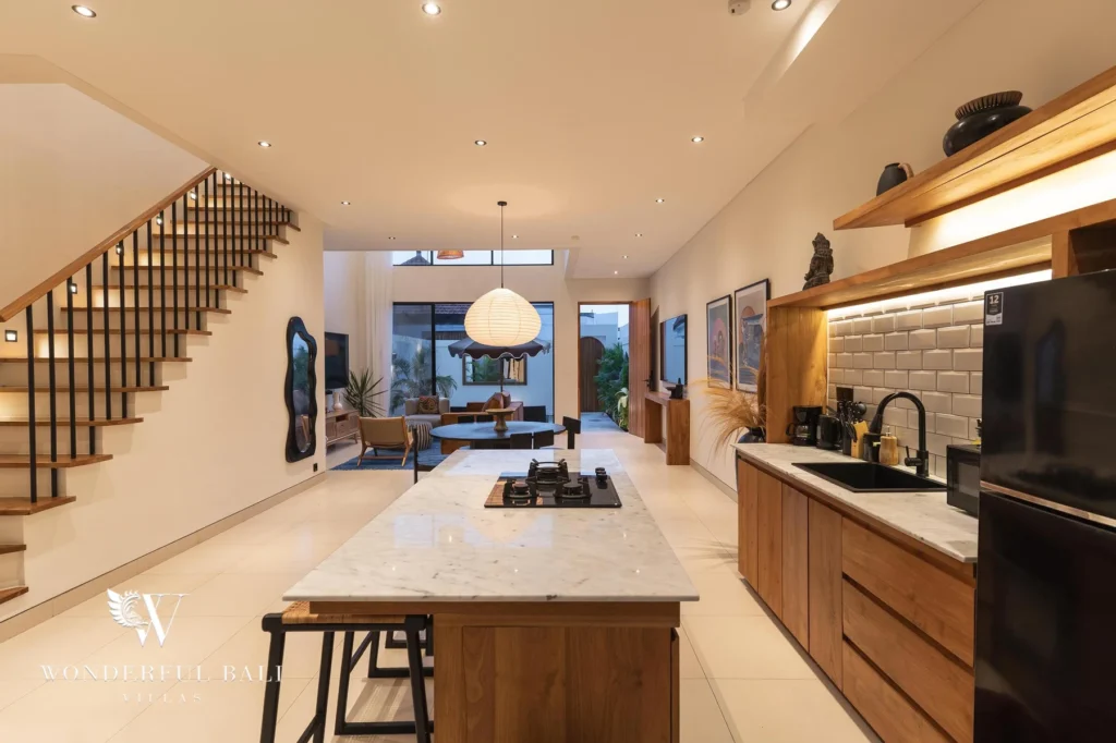 An open-plan interior at night with a marble kitchen island, staircase and lounge leading to the pool garden at a 2-bedroom villa in Canggu, Bali