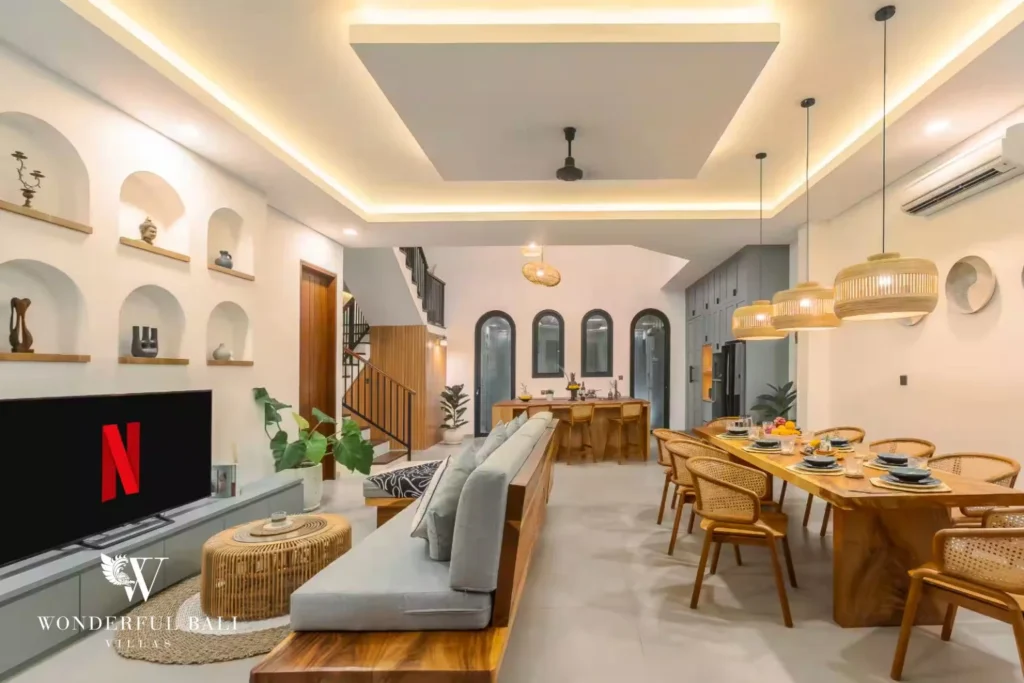 An open-plan living and dining space with grey sofa, long timber dining table and arched alcove wall at a 4-bedroom villa in Pererenan, Bali