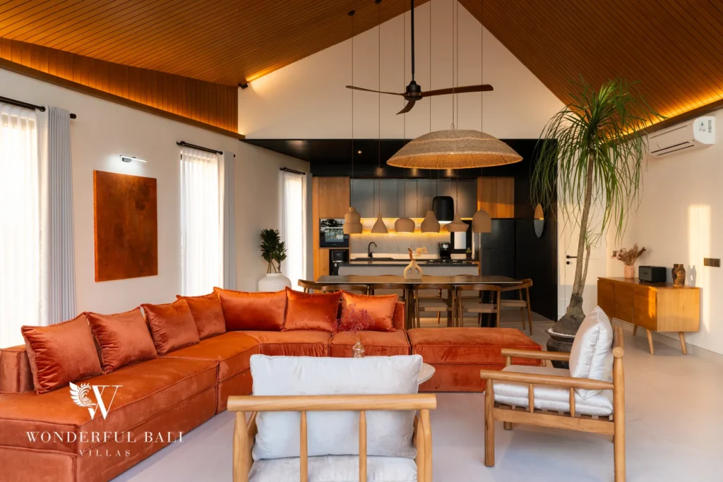 An open-plan living room with an L-shaped burnt-orange sofa, timber armchairs, a vaulted wood ceiling and a dining area and kitchen behind at a 5-bedroom villa in Batu Bolong, Canggu, Bali