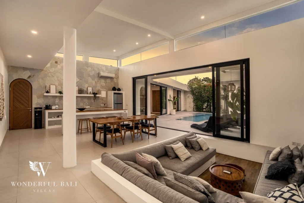 Spacious bathroom with a stone vanity, round mirror, rattan basket and a wooden arched door at a 3-bedroom villa in Bingin, Uluwatu, Bali