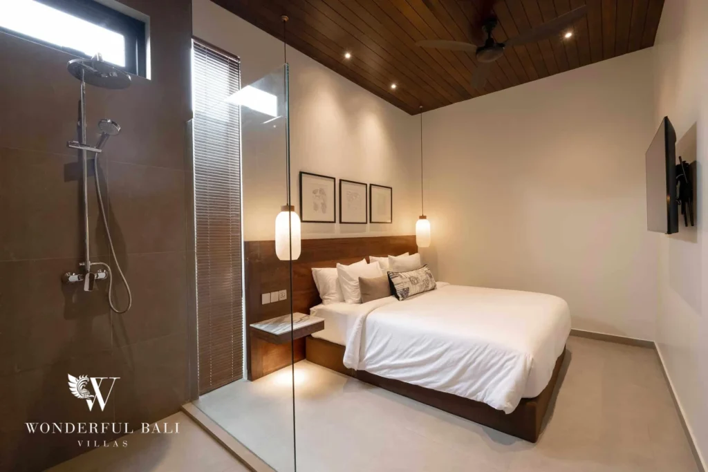 A bedroom with a glass-walled walk-in shower beside the bed under a warm wooden ceiling at a 2-bedroom villa in Canggu, Bali