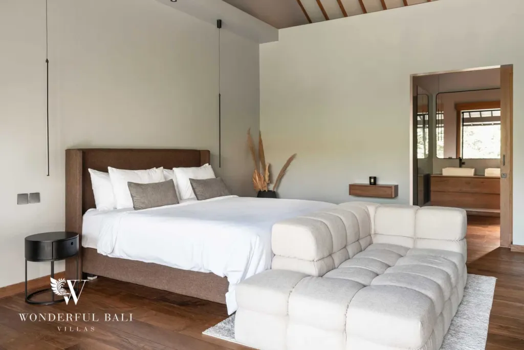 2BR villa for rent in Pererenan — bedroom, a bedroom with a brown upholstered bed, boucle daybed and pendant reading lights opening to an en-suite vanity beyond at a 2-bedroom villa