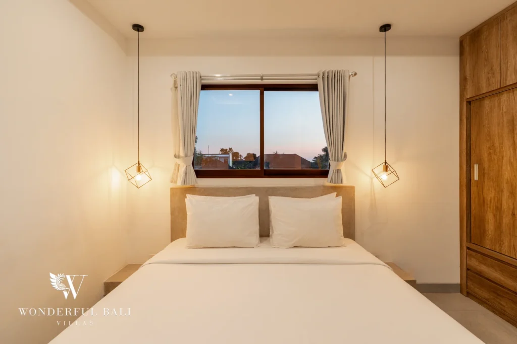 A bedroom with a double bed, geometric pendant lights and a window framing a rooftop sunset view at a 3-bedroom villa in Berawa, Bali