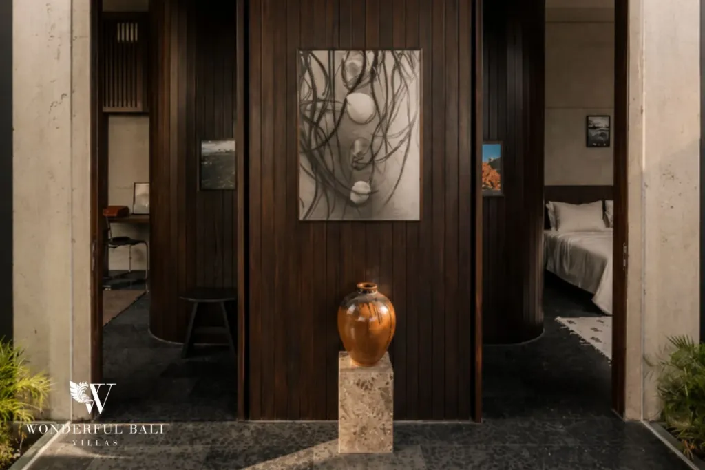 Timber-clad entry hall with framed artwork, a ceramic vase on a stone plinth and doorways opening to the bedrooms at a 2-bedroom villa in Seseh, Bali