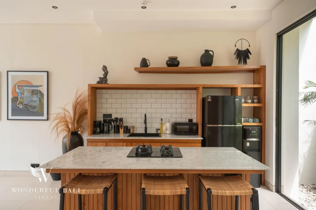 A fully equipped kitchen with a marble breakfast island, gas hob, subway-tile splashback and black fridge at a 2-bedroom villa in Canggu, Bali