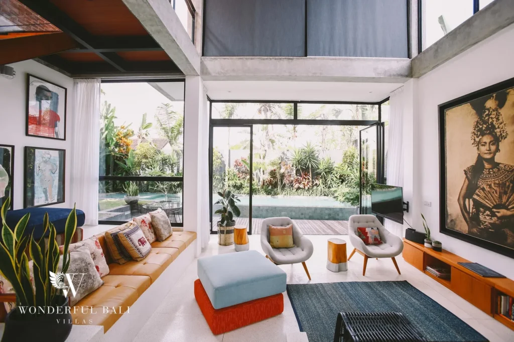 A double-height living room with a leather bench sofa, armchairs and floor-to-ceiling glass overlooking the pool and garden at a 4-bedroom villa in Batu Bolong, Canggu, Bali