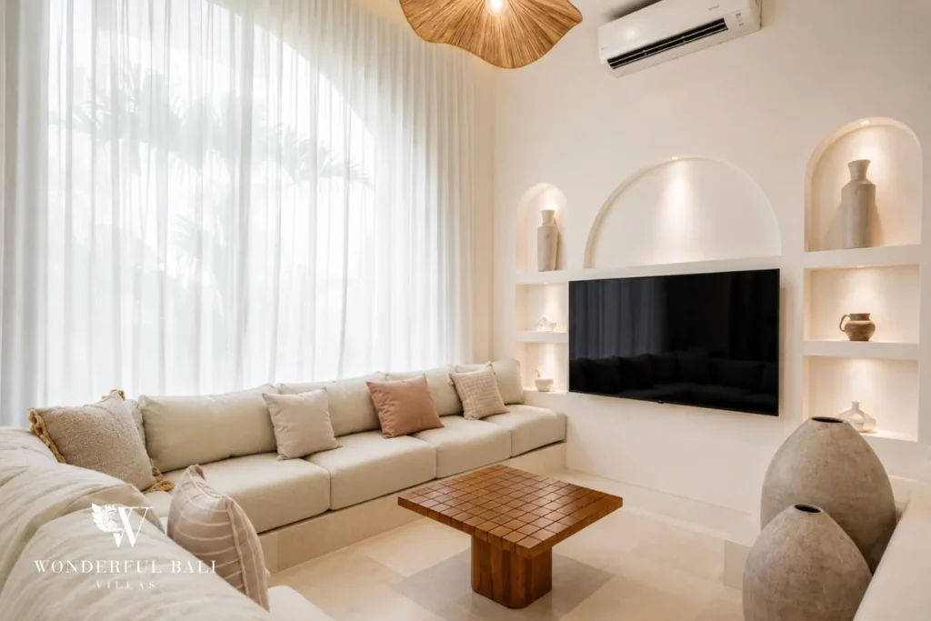 An enclosed air-conditioned sitting room with a cream sofa, TV set in a niche and lit display shelves, at a 2-bedroom villa in Bingin, Uluwatu, Bali